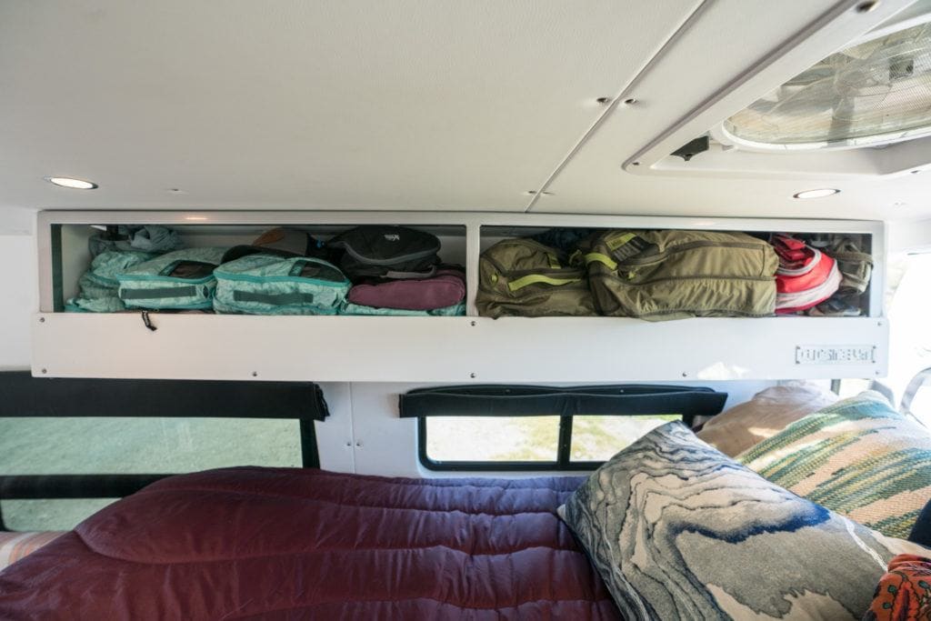 Photo of sleeping area in converted van with cabinets filled with clothes