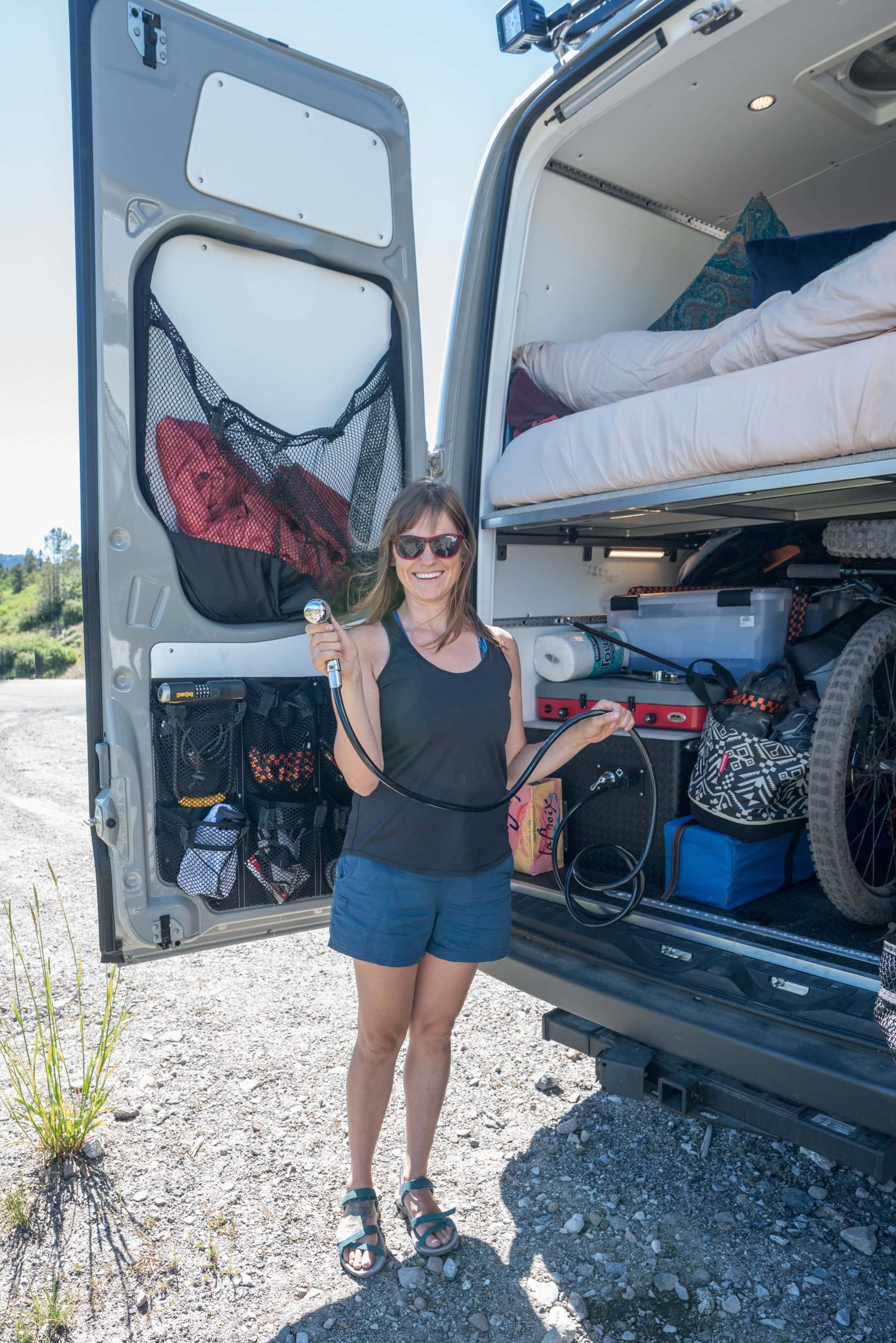 Kristen holding hose of van shower set up at rear of converted camper van