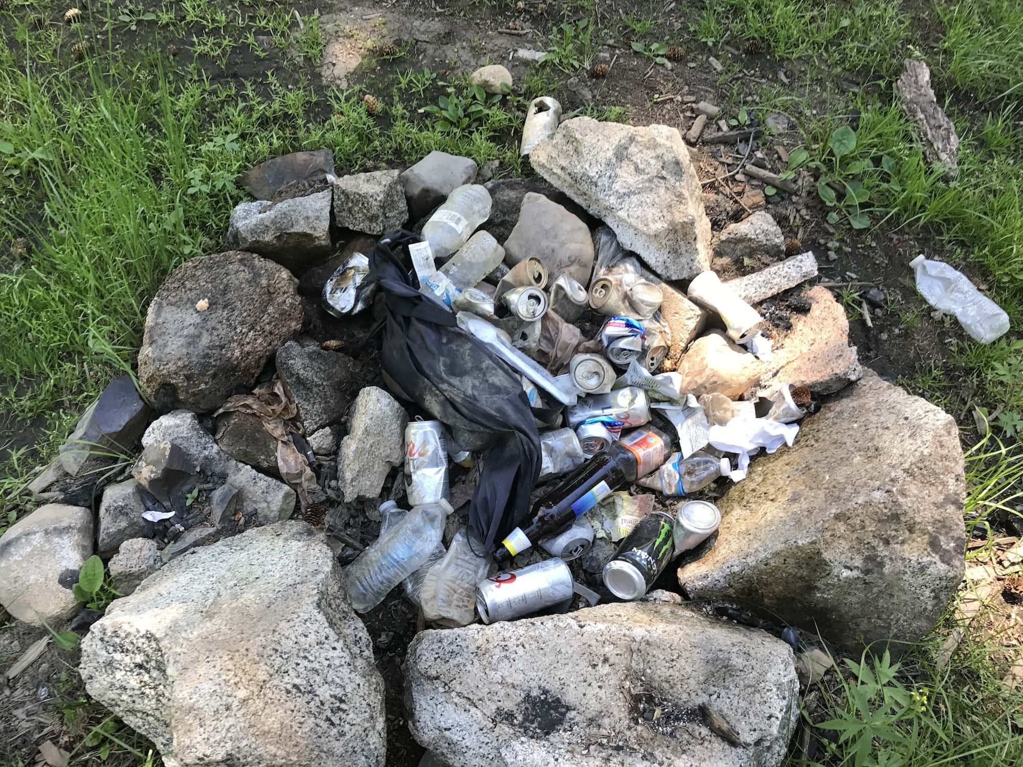 Trash including plastic bottles and beer cans in a fire pit surrounded by rocks