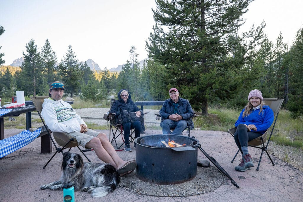 Four people sitting in camp chairs around fire pit at campsite