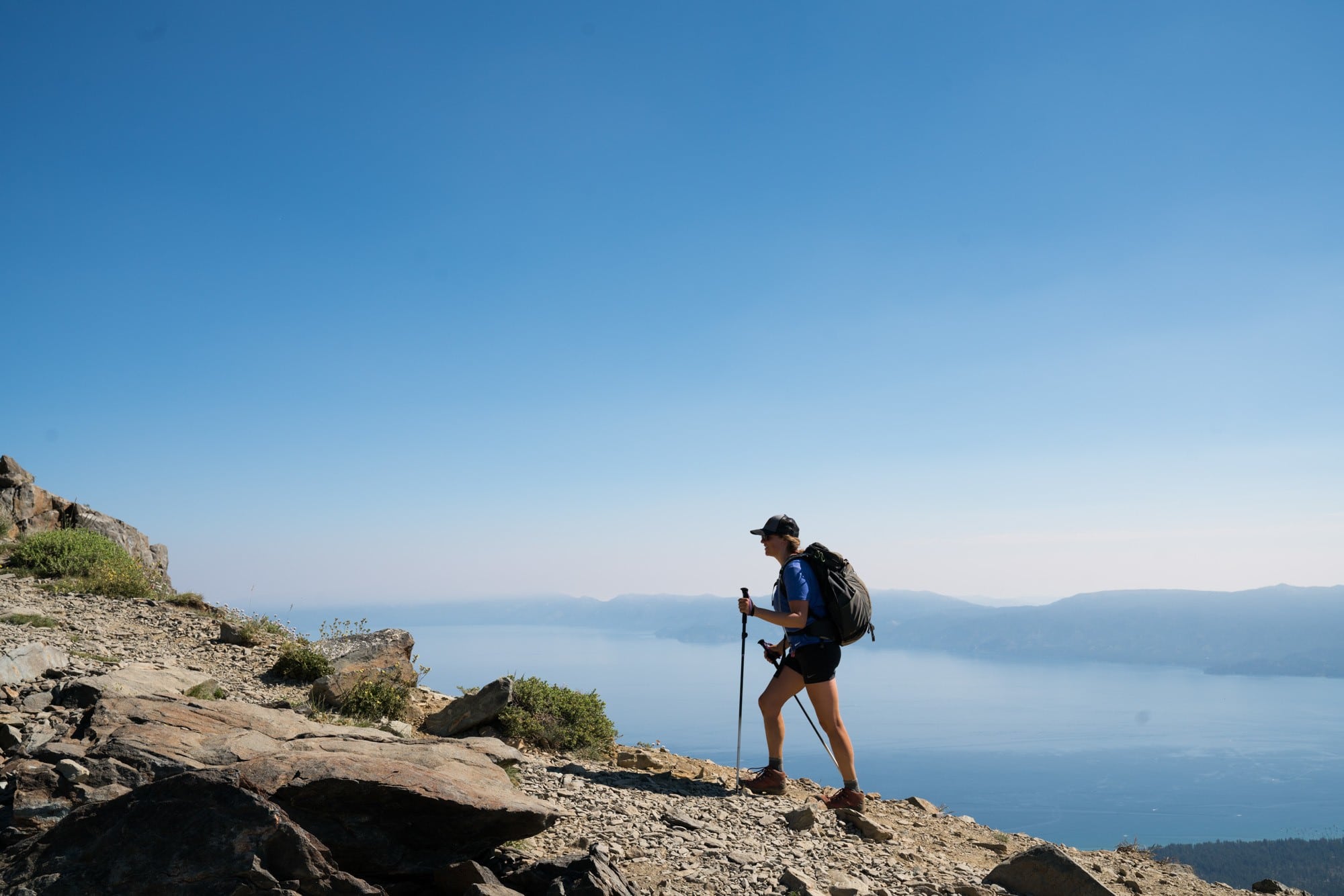 A woman using trekking poles hiking near a lake