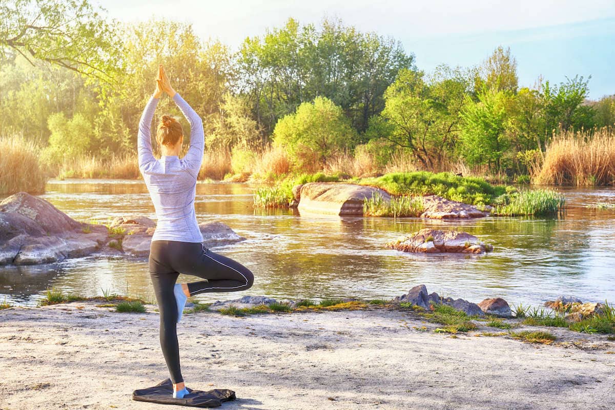 Woman doing yoga on sandy beach next to river