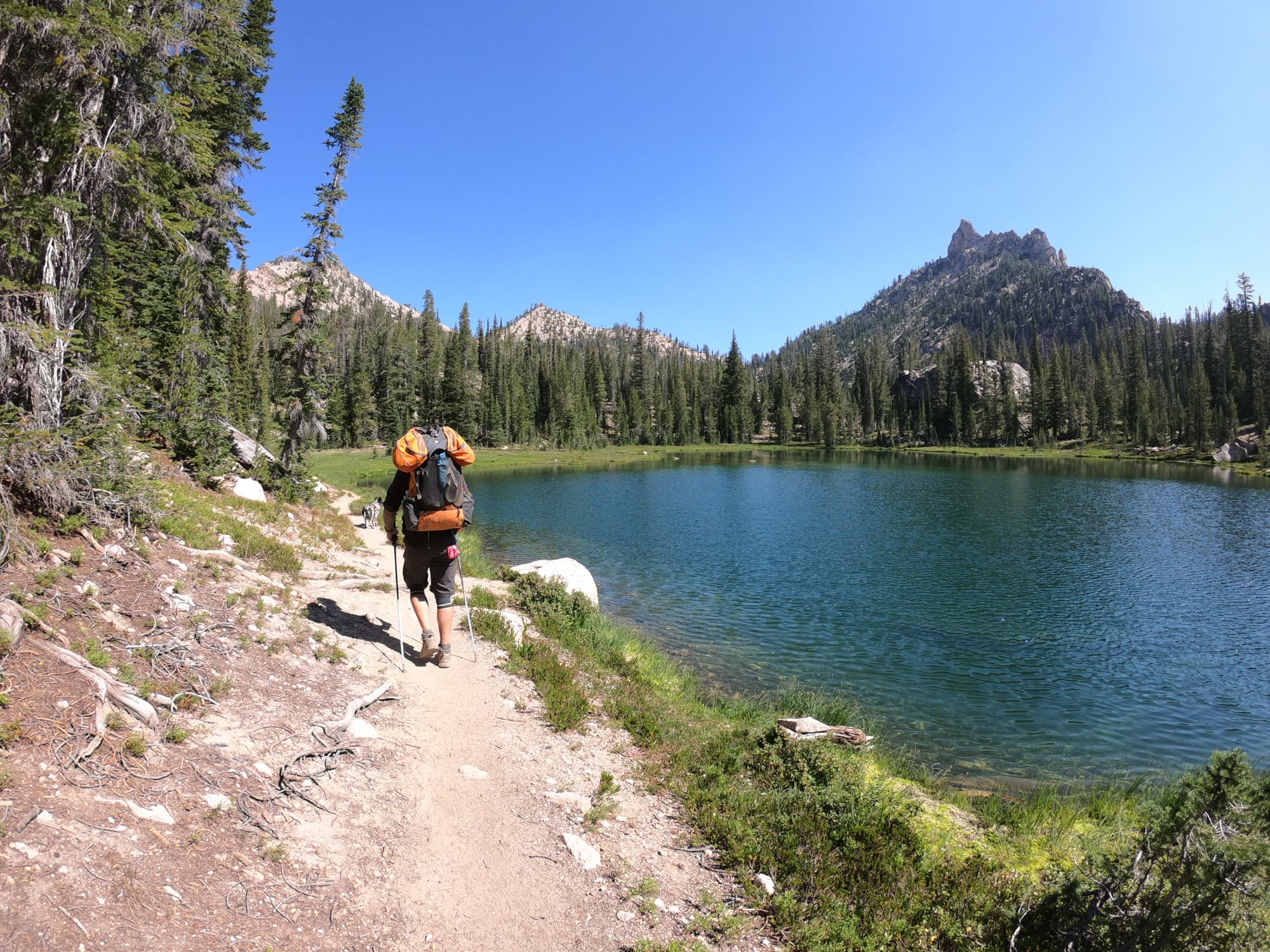 Man hiking on trail next to a small lake in Sawtooth Mountains in Idaho carrying a loaded backpacking backpack