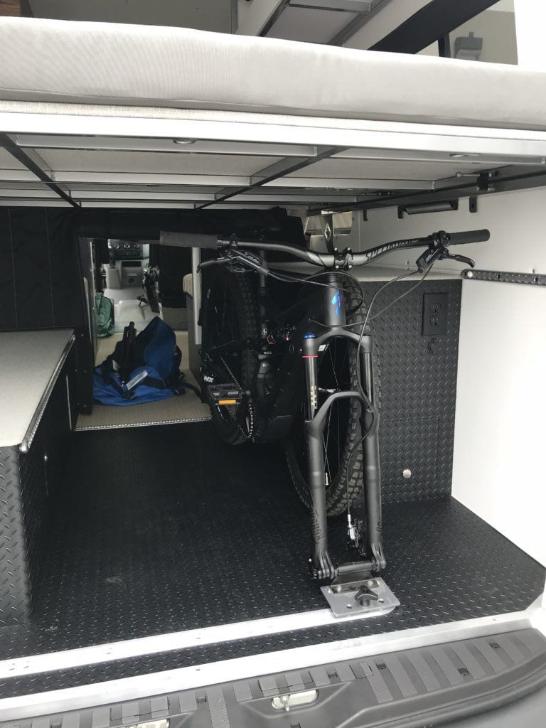 a bike in the garage of a camper van next to a caged in battery system