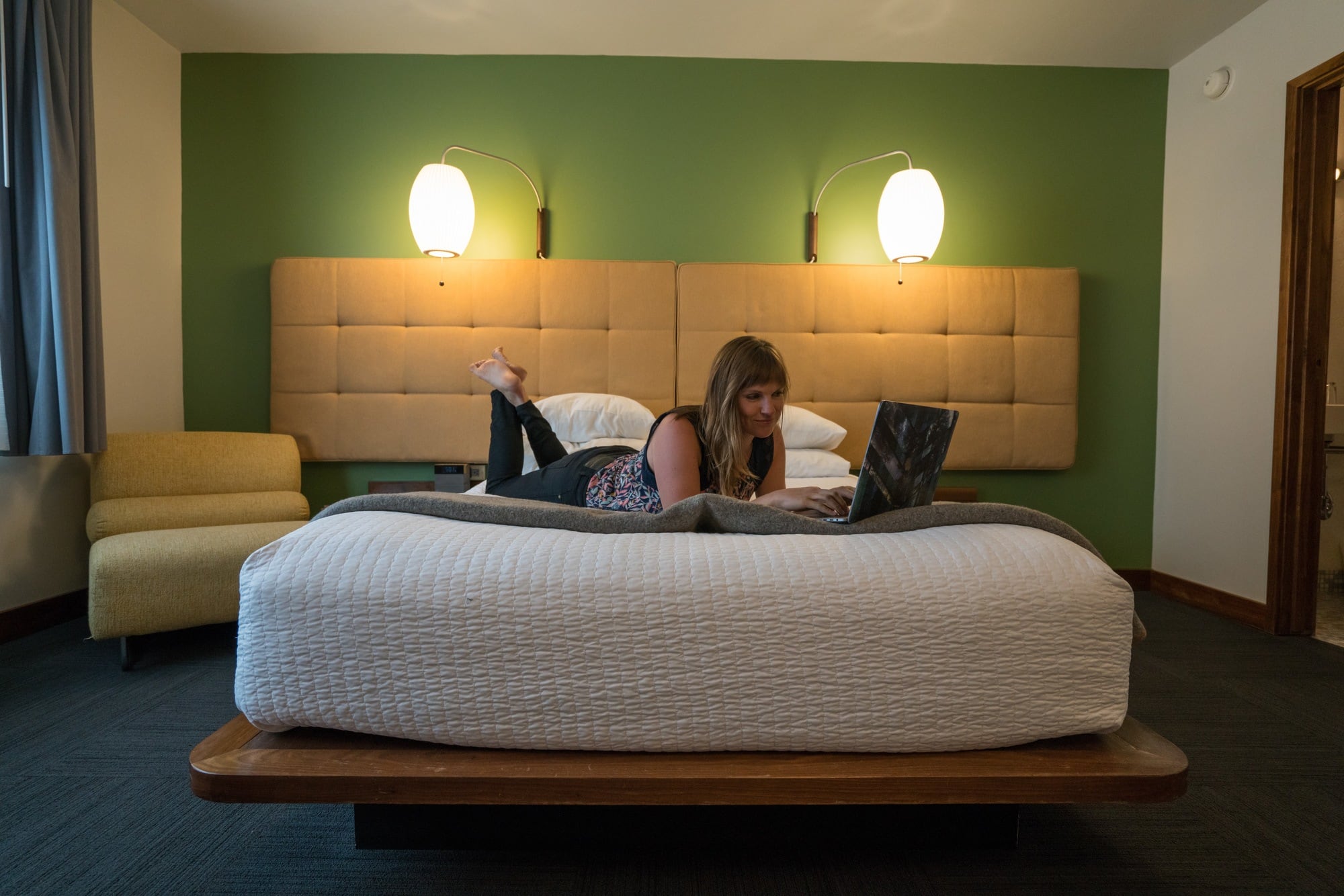 Kristen Bor sitting on a bed working on a computer at the Modern Hotel in Boise