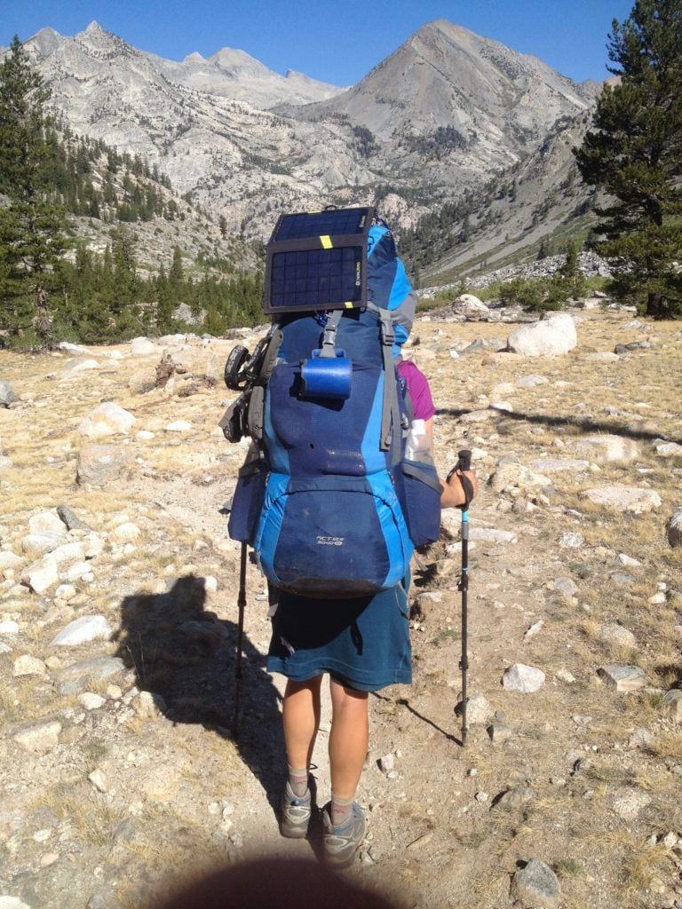 A woman wearing a large backpacking pack on the John Muir Trail. There's a solar panel hanging off the pack