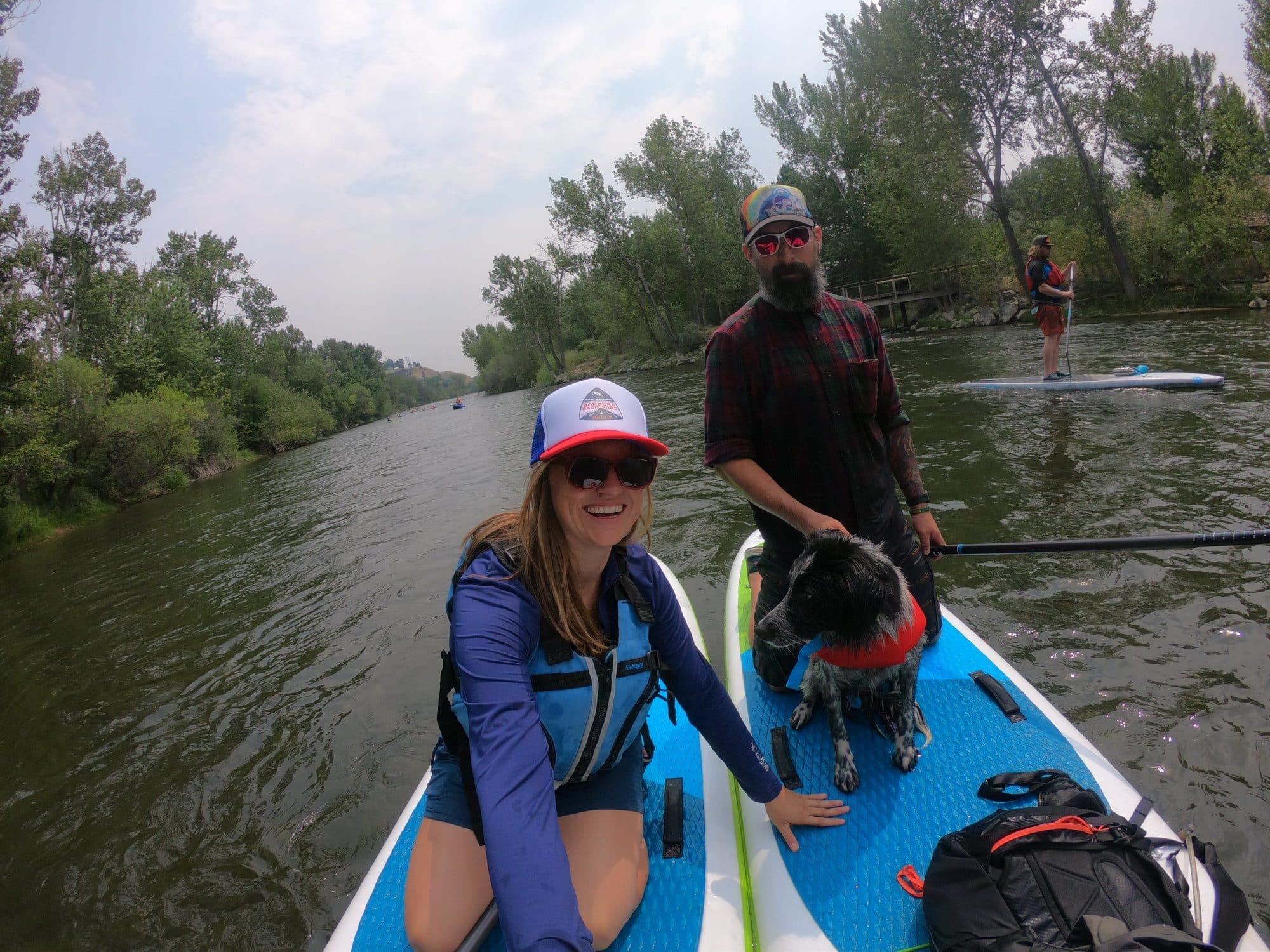 Kristen Bor and a man with a dog sitting on paddle boards in a river