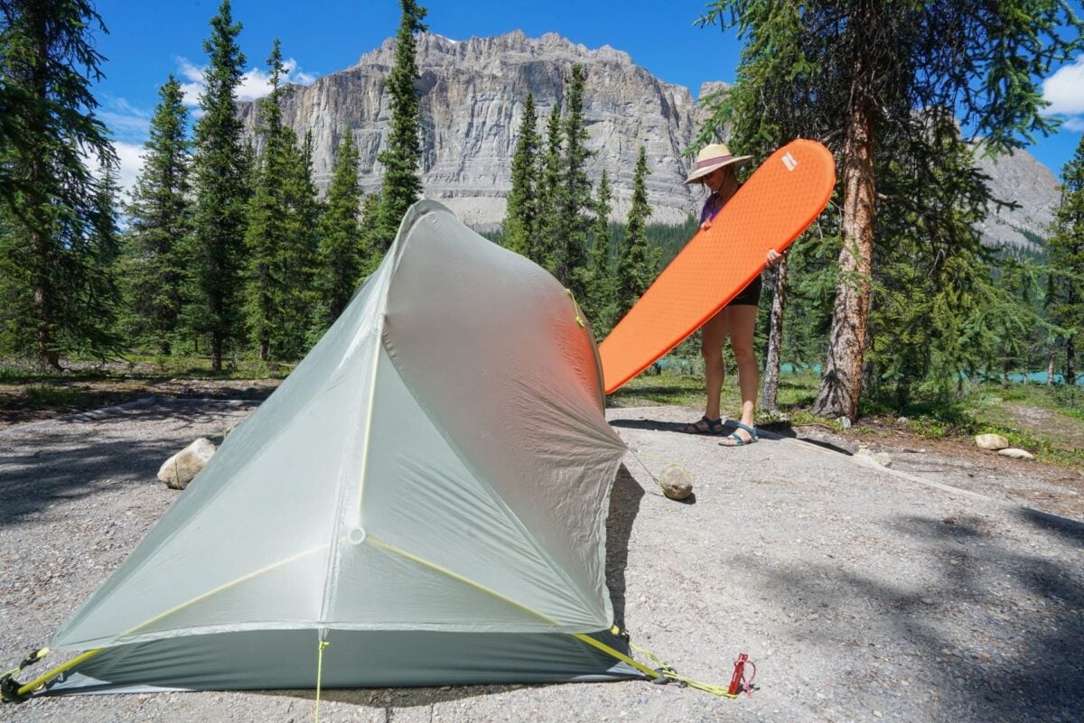 Kristen Bor putting a Therm a Rest Sleeping Pad into a tent with a mountain and trees in the background