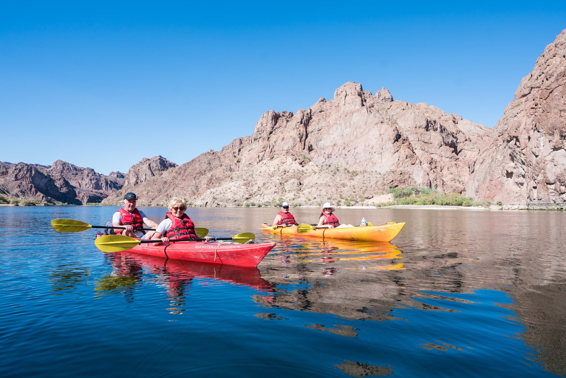 Two older couples sit in tandem kayaks. One is red and the other is yellow.