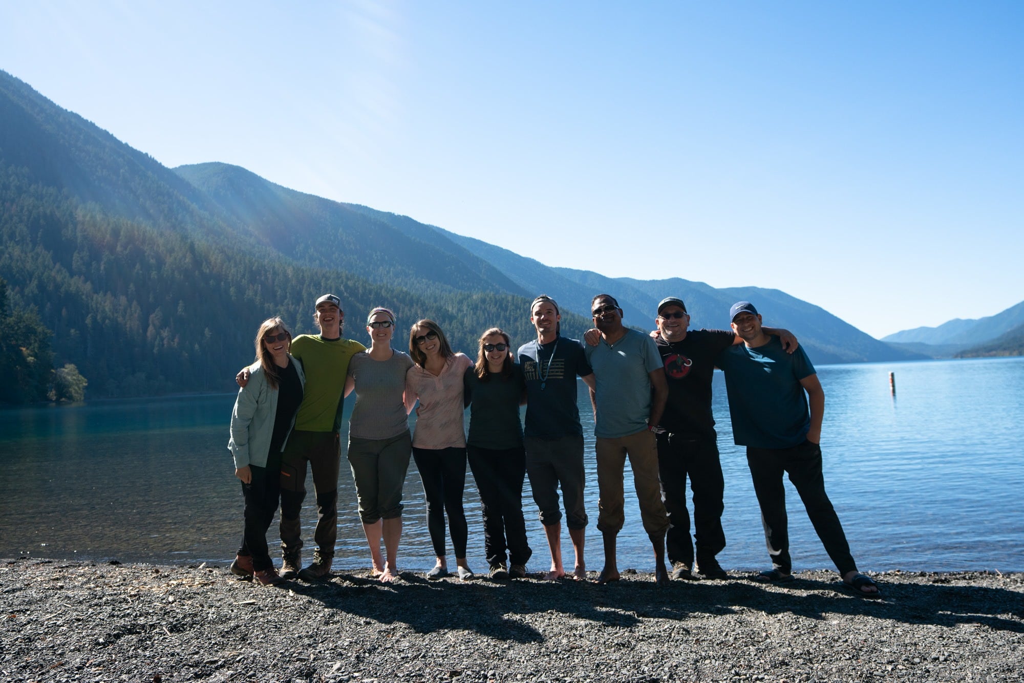 Nine people standing side by side with arms around shoulders in front of Crescent Lake in Washington