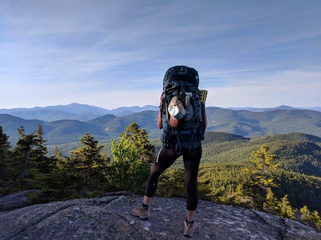 Woman carrying heavy backpacking pack looking out at mountain views from the Carter Ledge Loop in New Hampshire