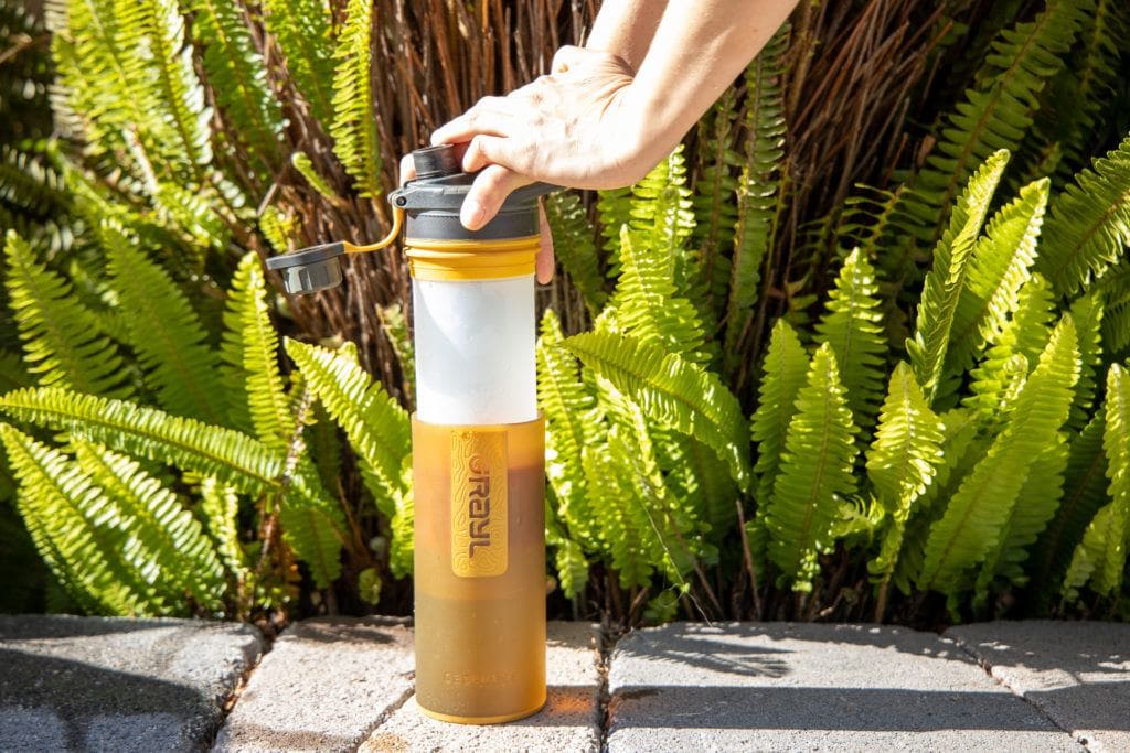 A woman pressing down the Grayl Geopress water bottle to filter cleaning drinking water. 