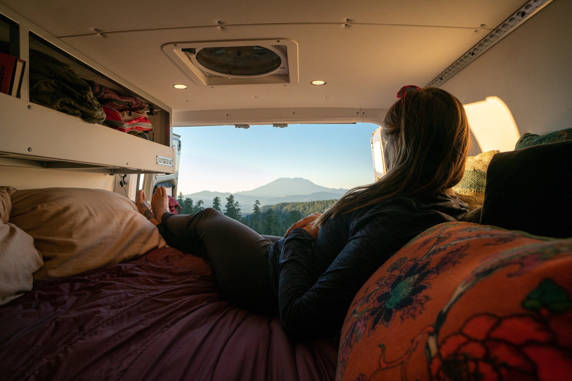 Kristen Bor lying on a Rumpl blanket in the bed of her Sprinter Van with Mt St Helens in the background