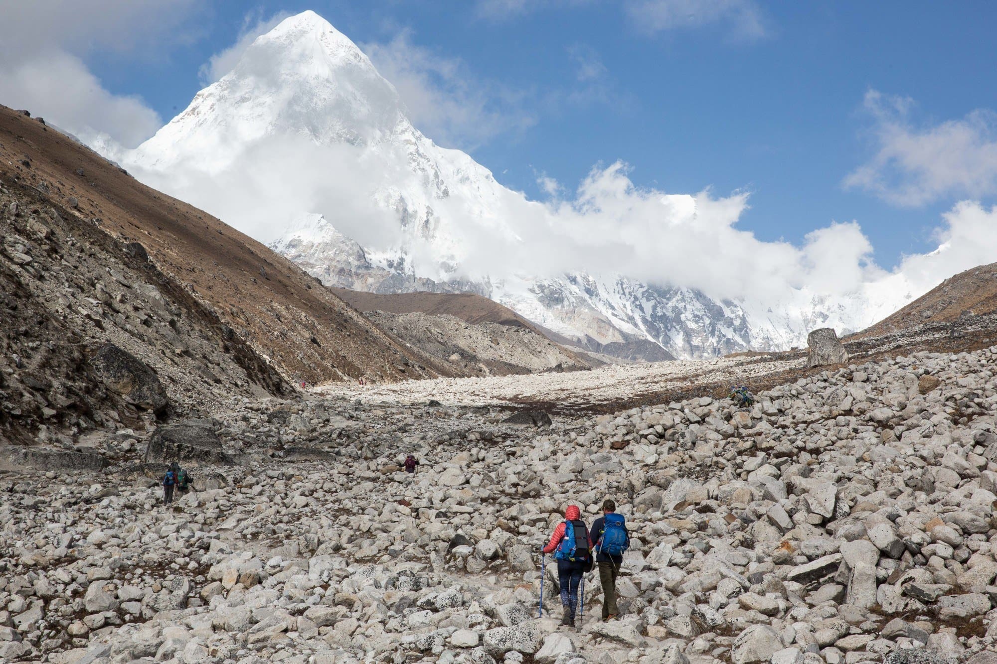 Two hikers hiking over rock field with snow-capped mount Everest looming above them