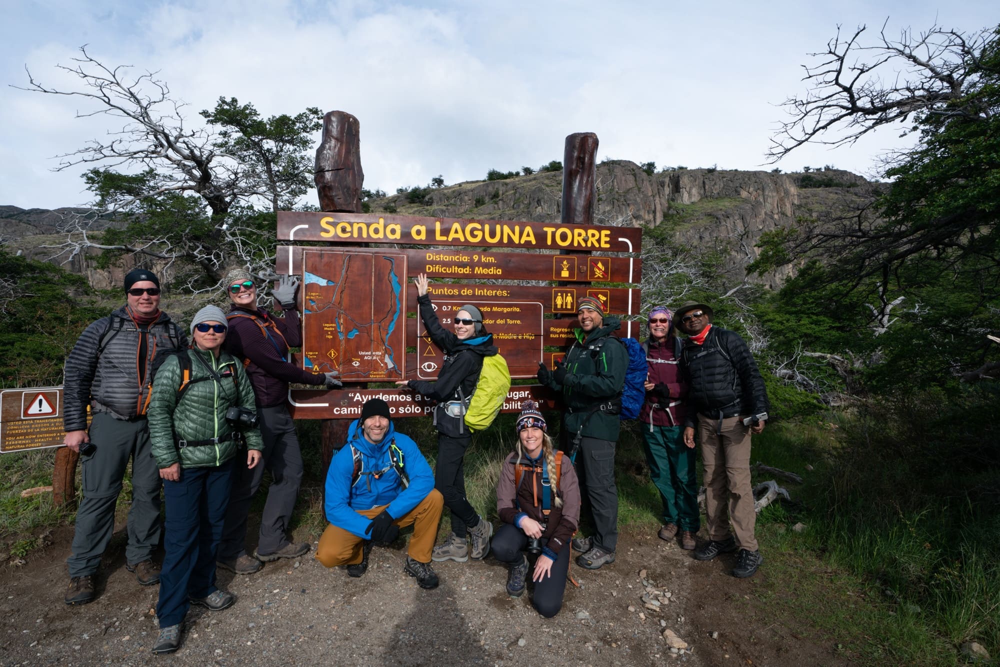 Group of hikers dressed in warm layers in front of a trail sign for Senda a Laguna Torre hike in Patagonia