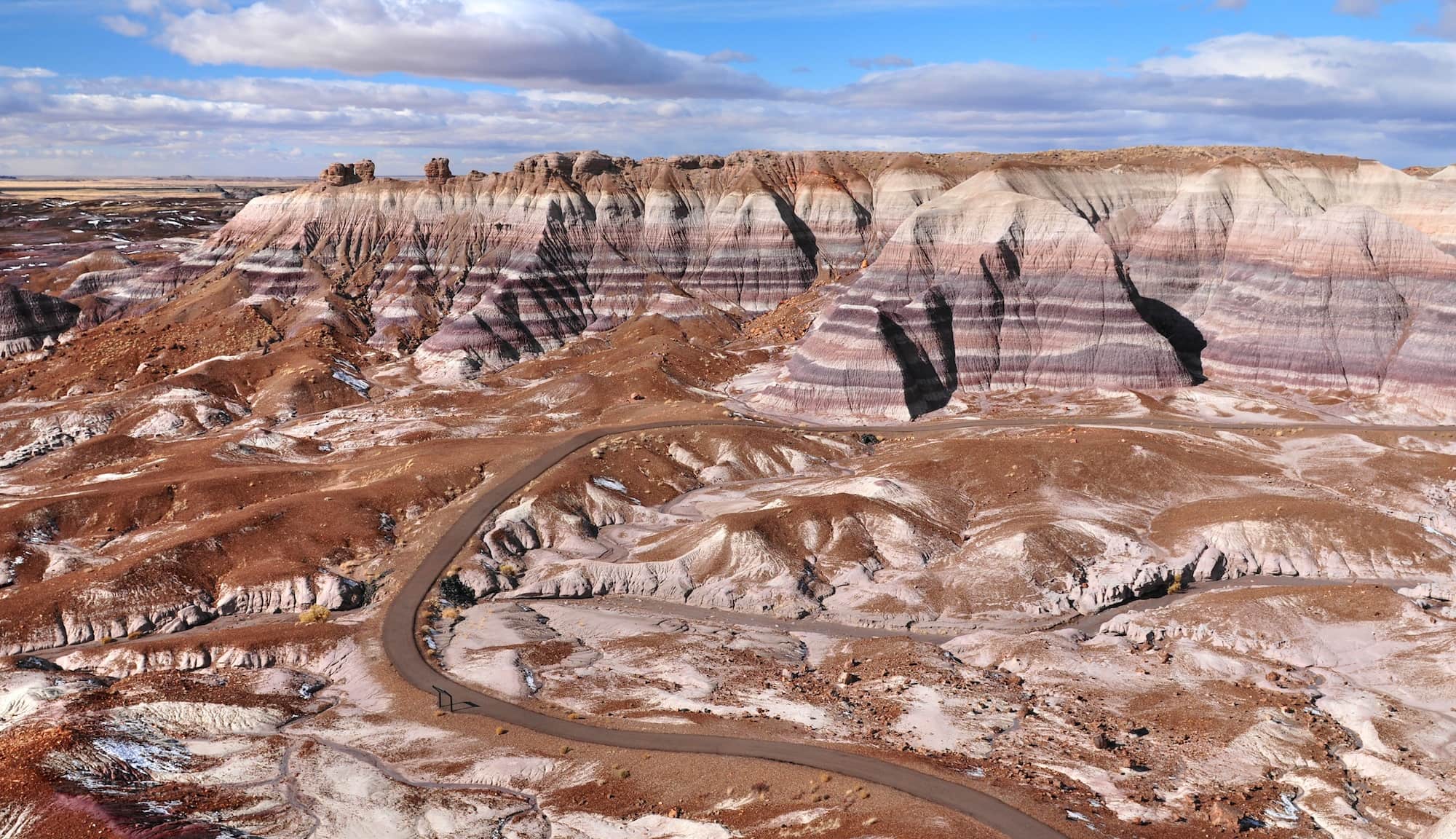 Panoramic views of badlands and stratified bluffs in Petrified Forest National Park in Arizona with windy road running through landscape