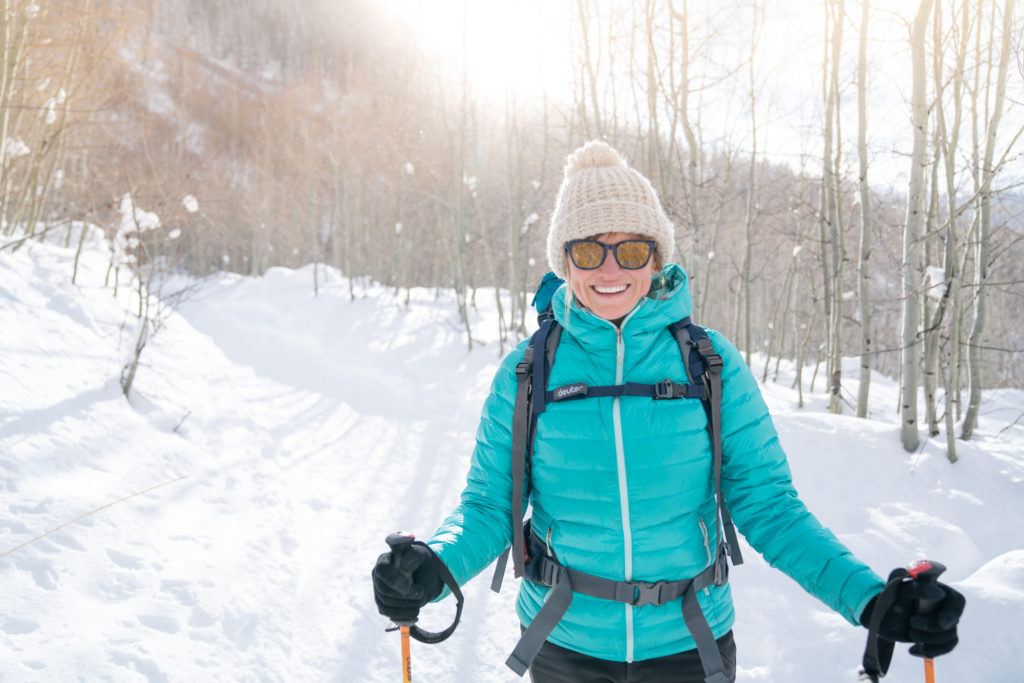 A woman smiles wearing winter suit while snowshoeing