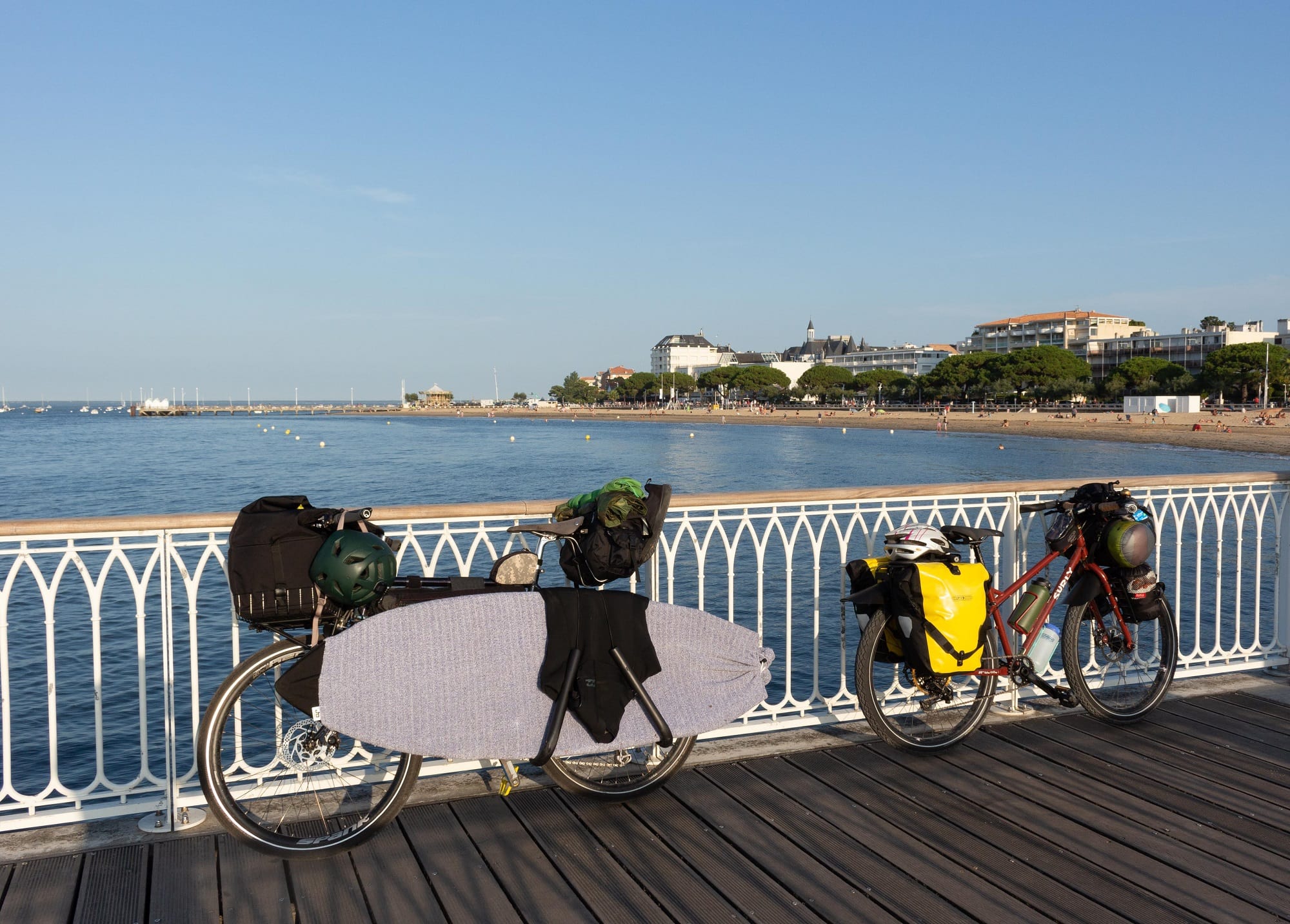Two bikes loaded with bike touring gear leaning against railing with ocean bay in background