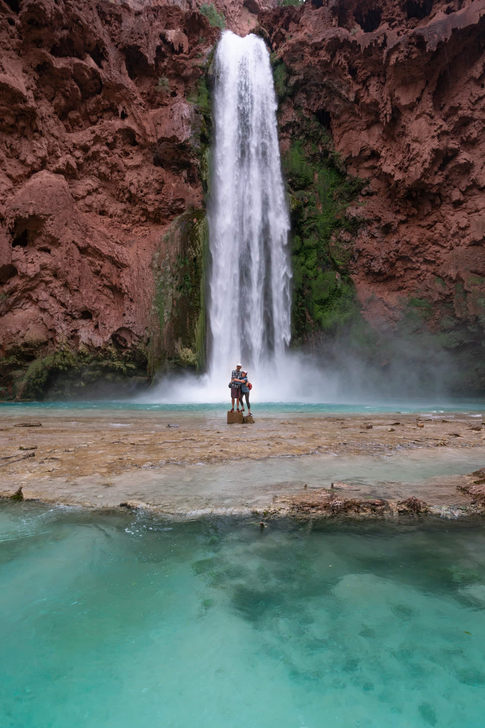 A couple getting their photo taken in front of Mooney Falls in Havasu Canyon, Arizona