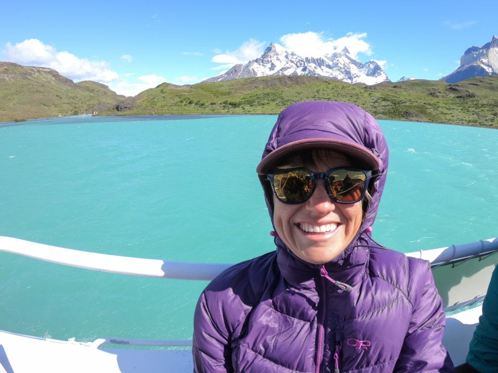 Photo of woman on deck of boat with blue lake and snow-capped mountain behind her