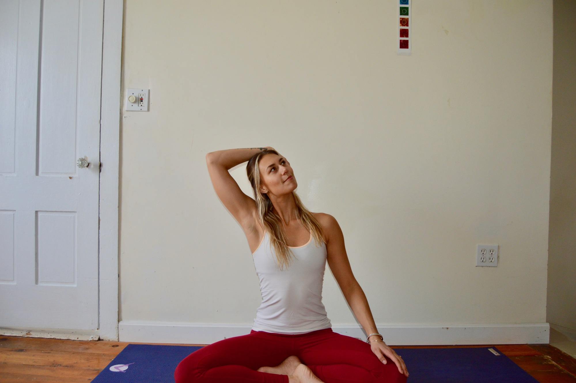 Woman sitting on a yoga mat gently stretching her neck / One of our favorite yoga poses for skiers