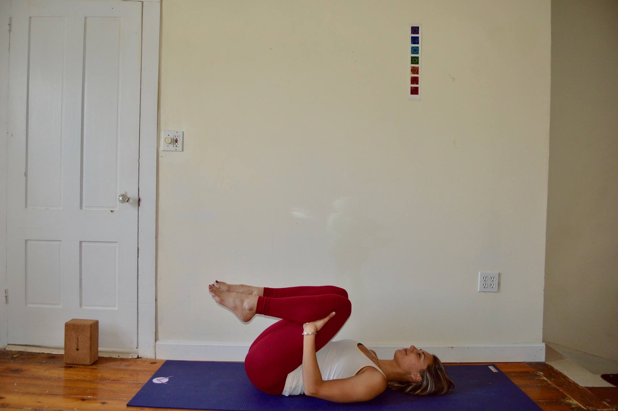 Woman laying on her back on a yoga mat with her legs tucked in, demonstrating yoga for skiing