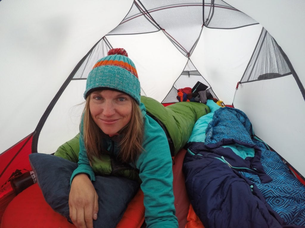 Kristen Bor lying on her stomach looking at the camera in a tent inside her sleeping bag