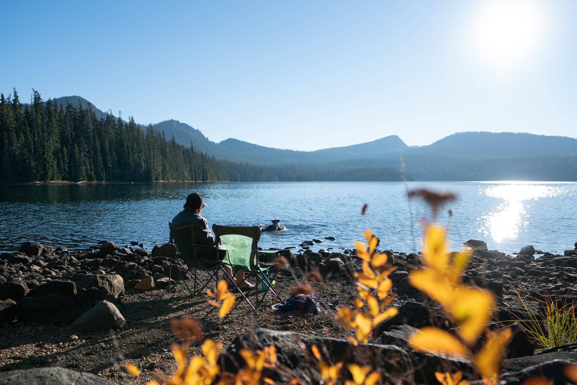 A person sits in a camp chair next to a lake on a road trip