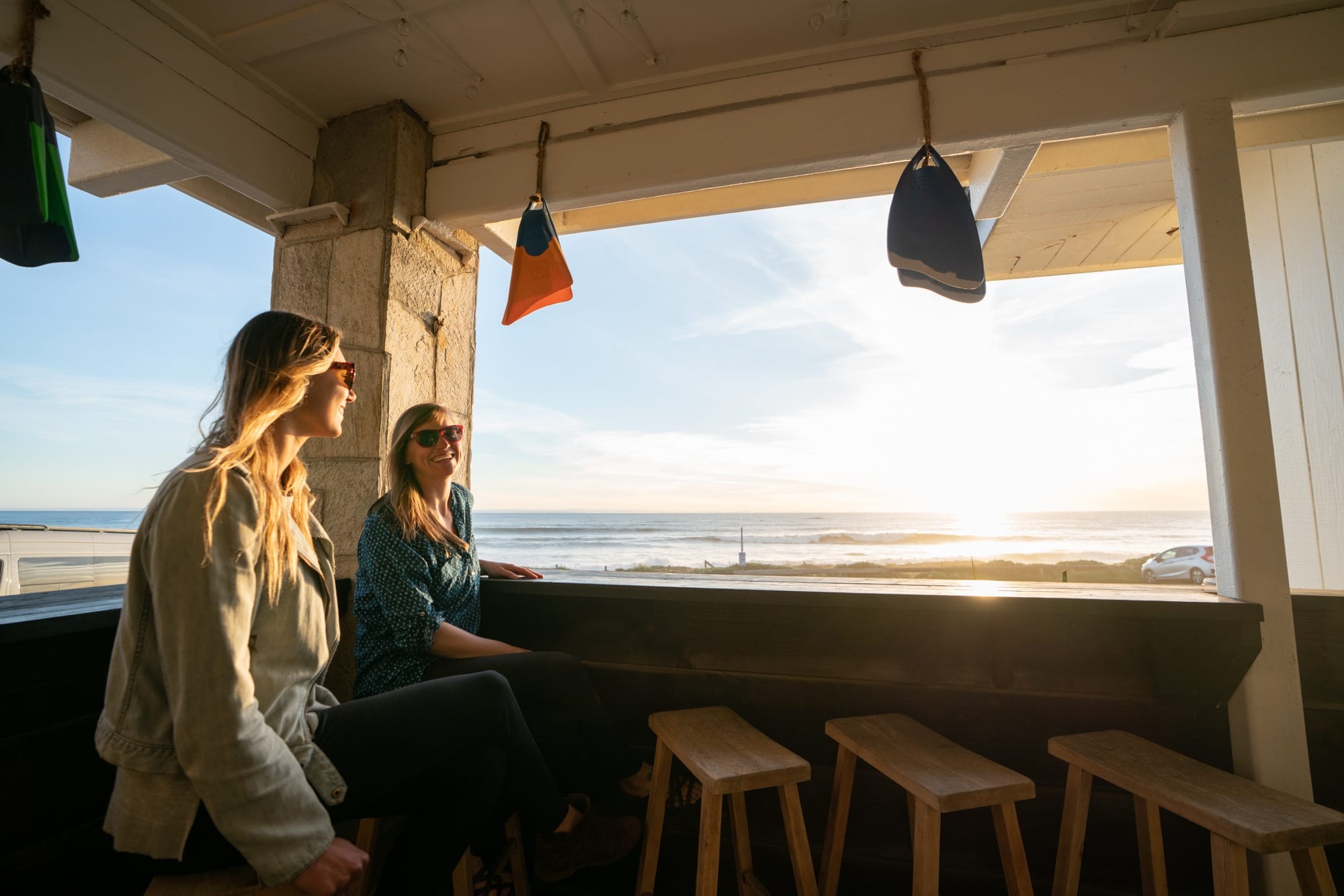 Two women sitting at unshut bar zone next to a waterfront in California