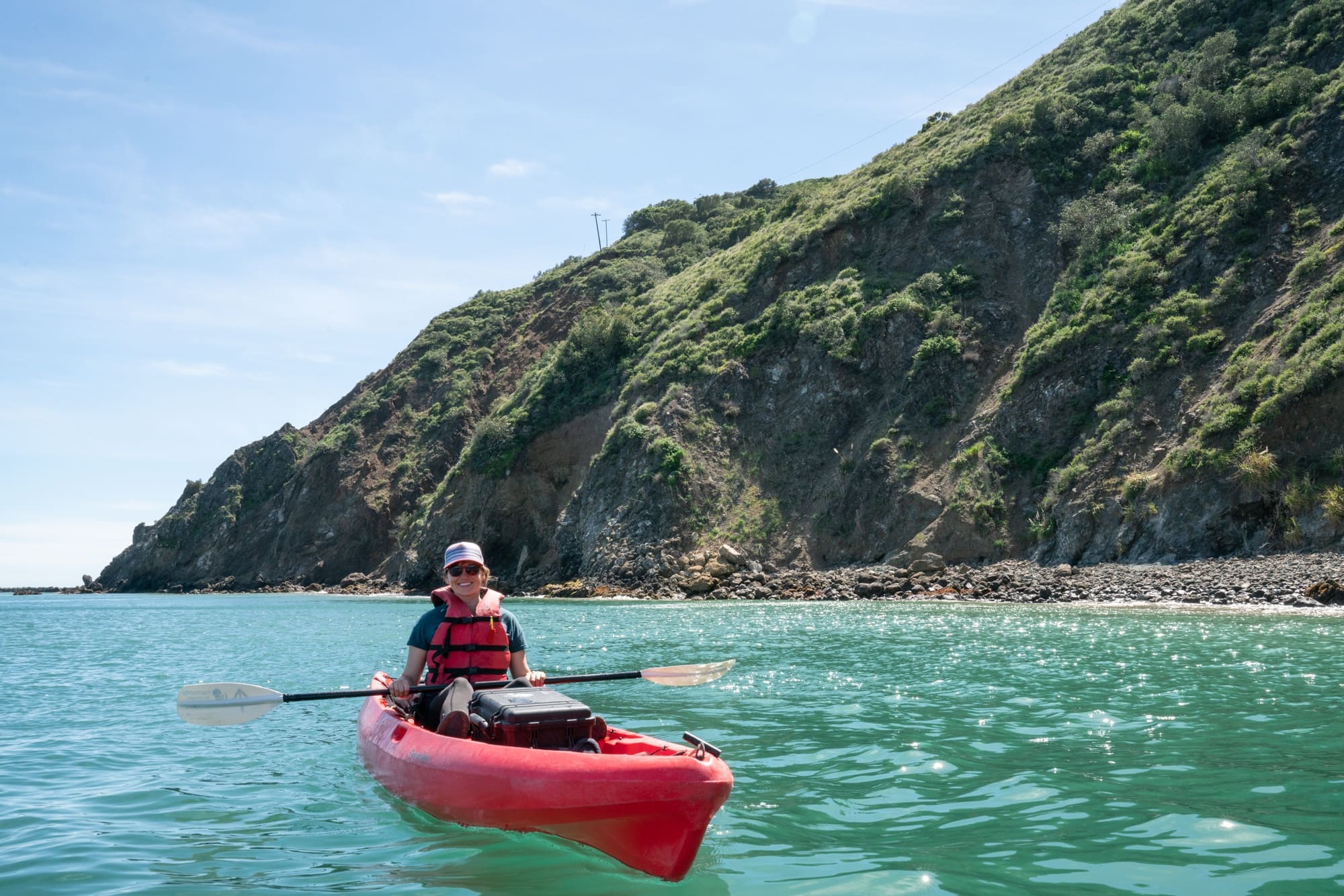 Woman sitting in kayak on the water with steep, rugged cliffs on one side