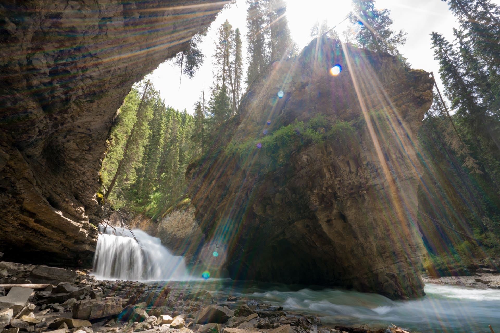 A waterfall cascades down with a sunbeam in Johnston Canyon in Banff