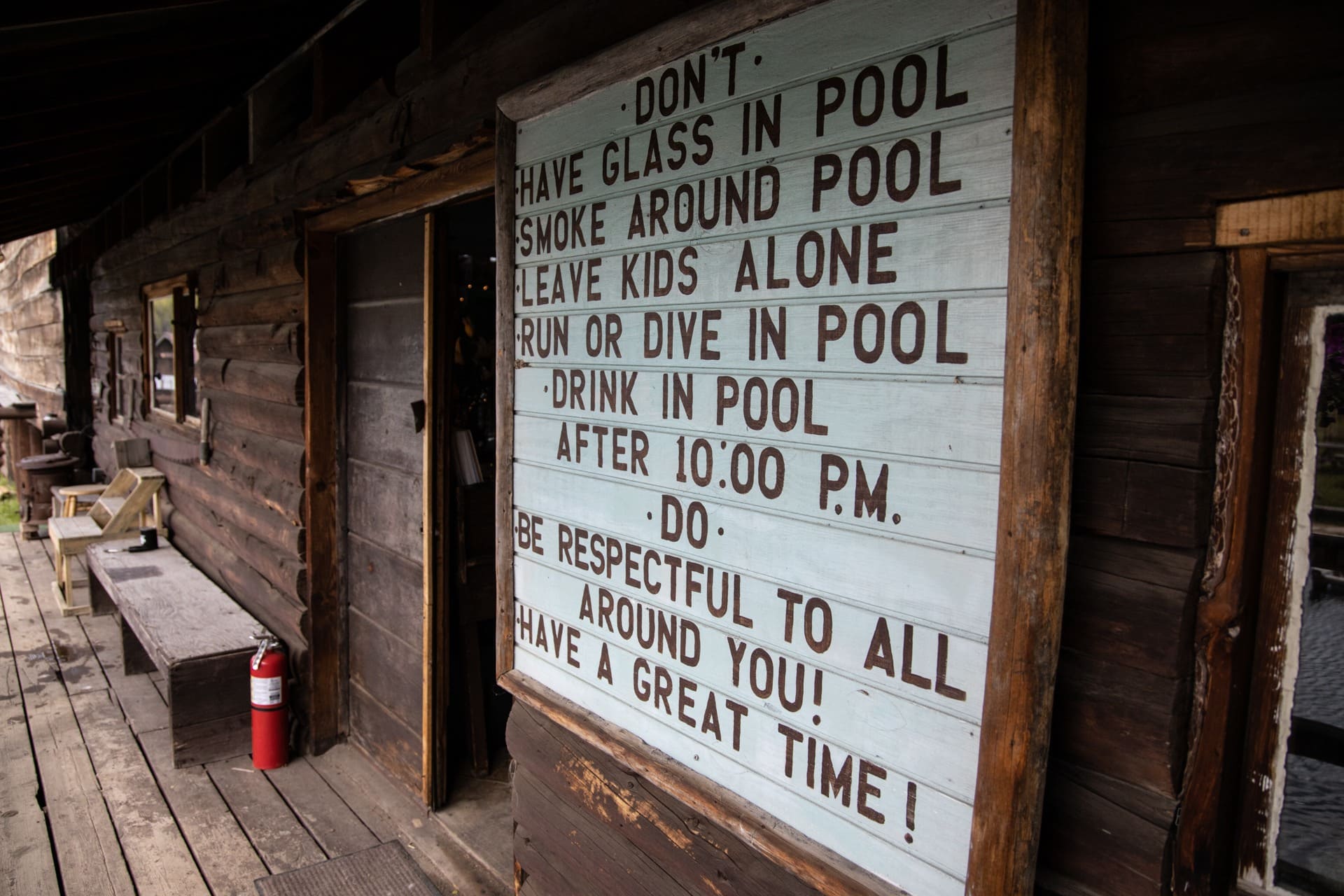 Sign on historic wooden building at Burgdorf Hot Springs that says "Don't have glass in pool smoke around pool leave kids along run or dive in pool drink in pool after 10:00 pm. Do be respectful to all around you! Have a great time!"