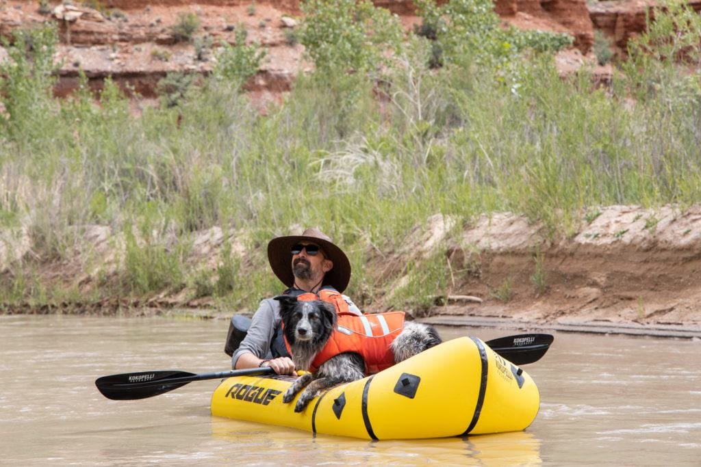 Man in packraft with dog floating on river