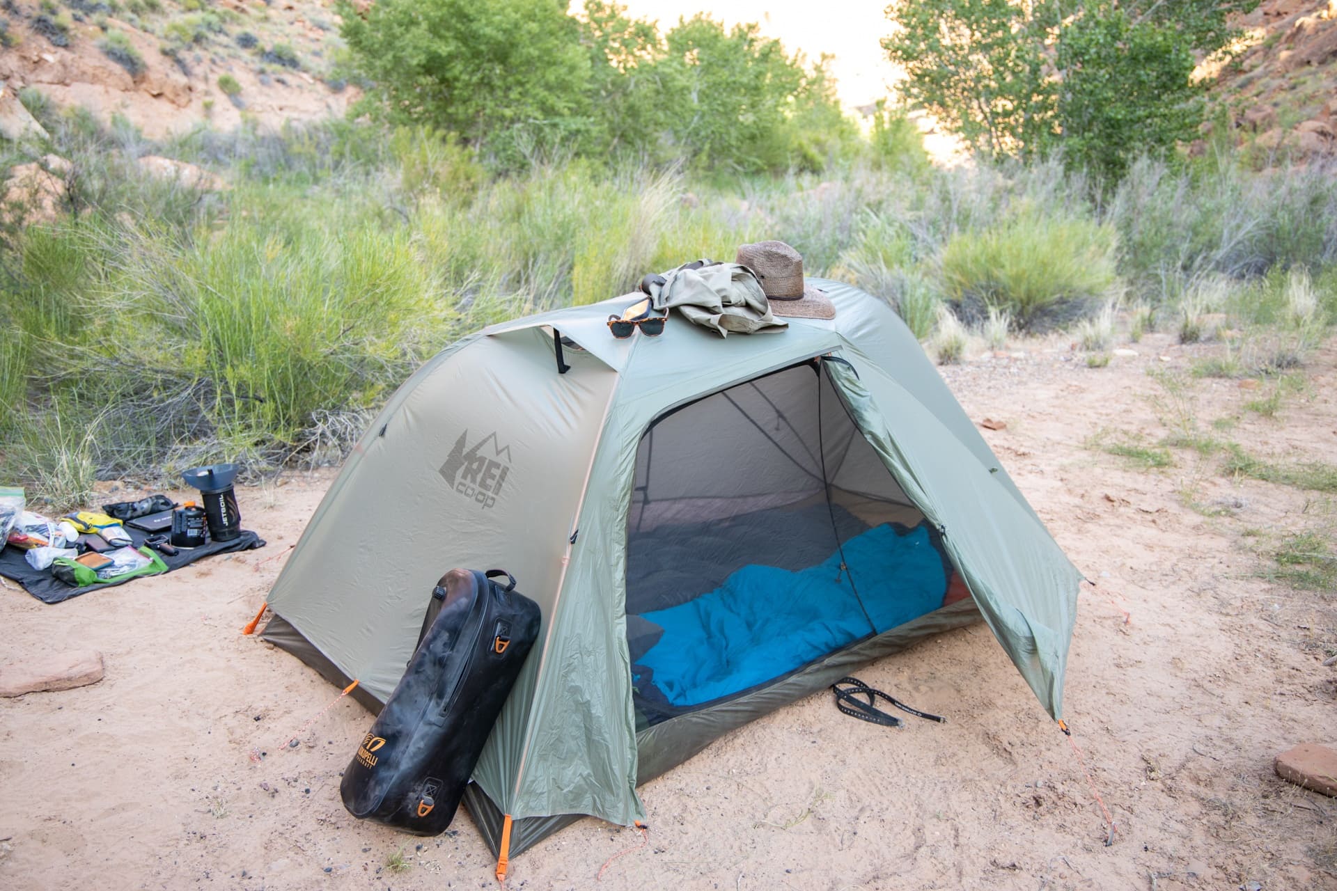 The REI Quarter Dome SL 2 tent set up on a sandy clearing in a Utah canyon with shrubs and trees in the background.