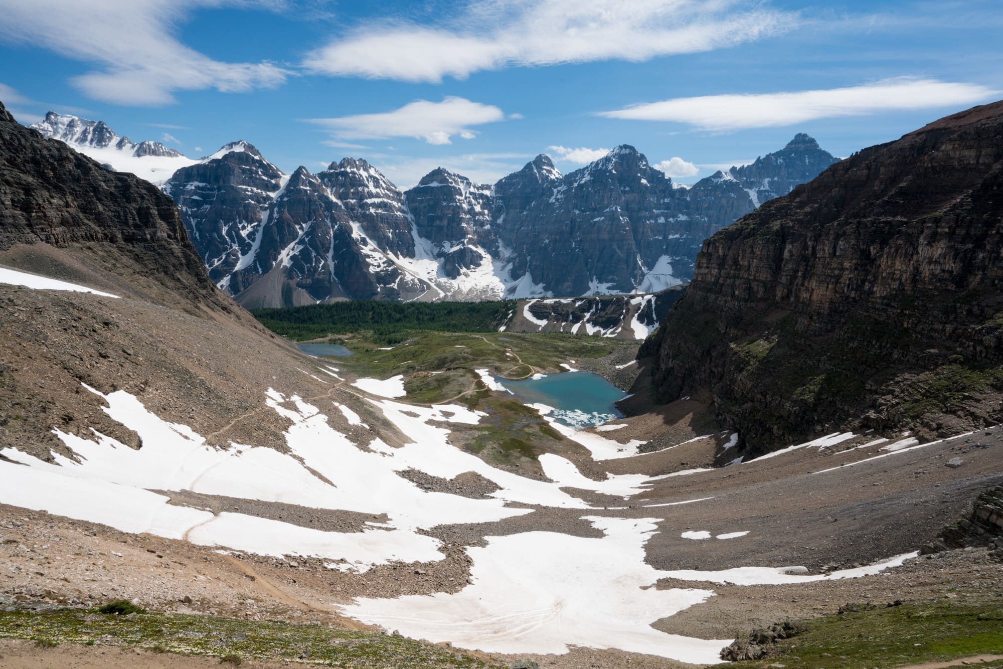 Looking down at Lake Moraine from the Sentinel Pass Trail with patches of snow and bright blue water at the bottom