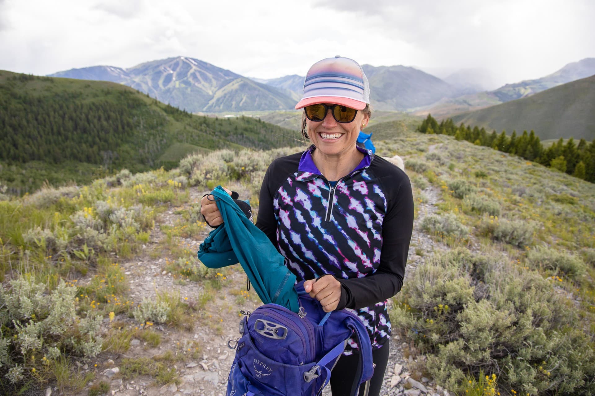 Kristen on hiking trail pulling an extra layer from her backpack