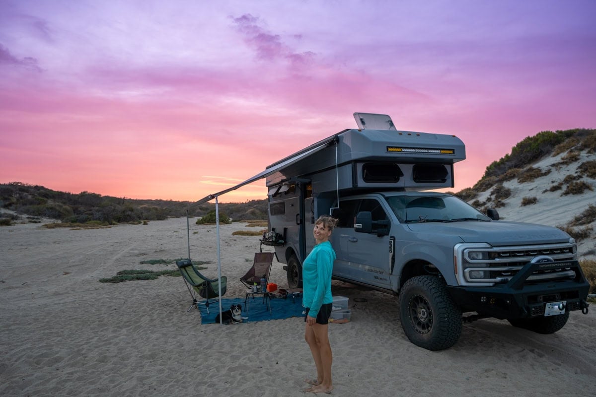 Kristen Bor standing next to Rossmonster Baja Trail adventure truck on sandy beach in Baja at sunset