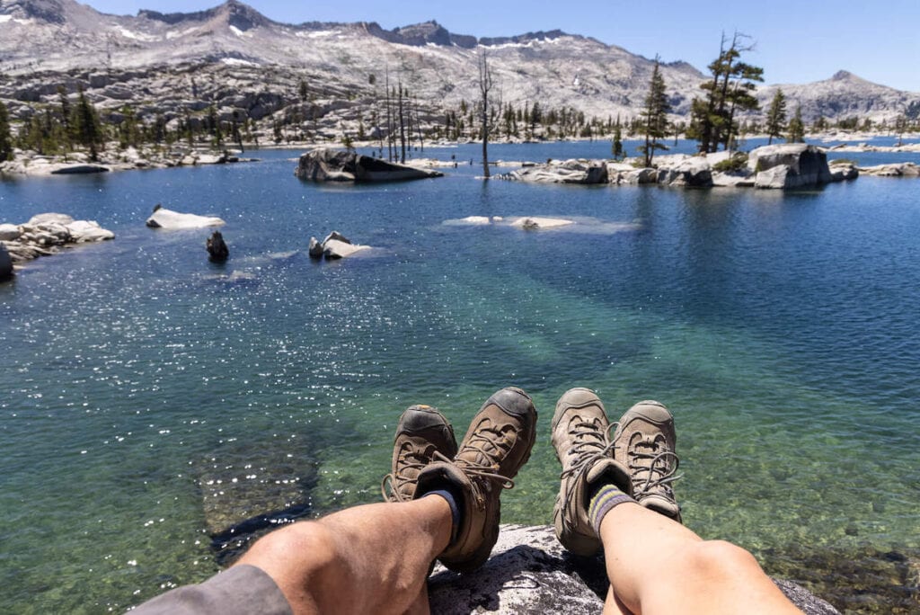 Photo out over two hikers legs and feet sitting on rock in front of Desolation Wilderness Lake in California wearing Oboz hiking boots