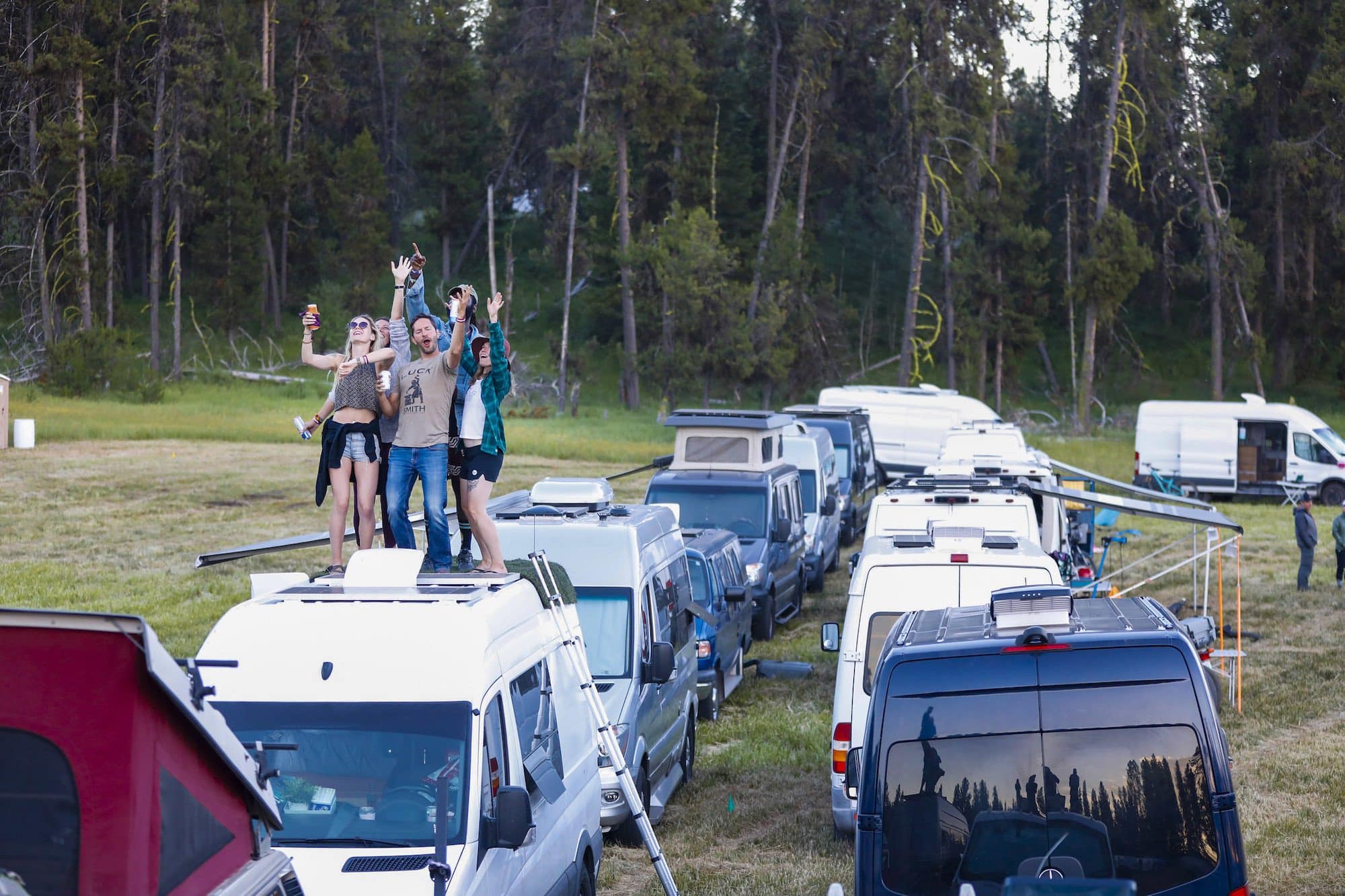 A group of people dancing on top of the roof of a van at sunset during Open Roads Fest, a van life festival and campout in McCall, Idaho