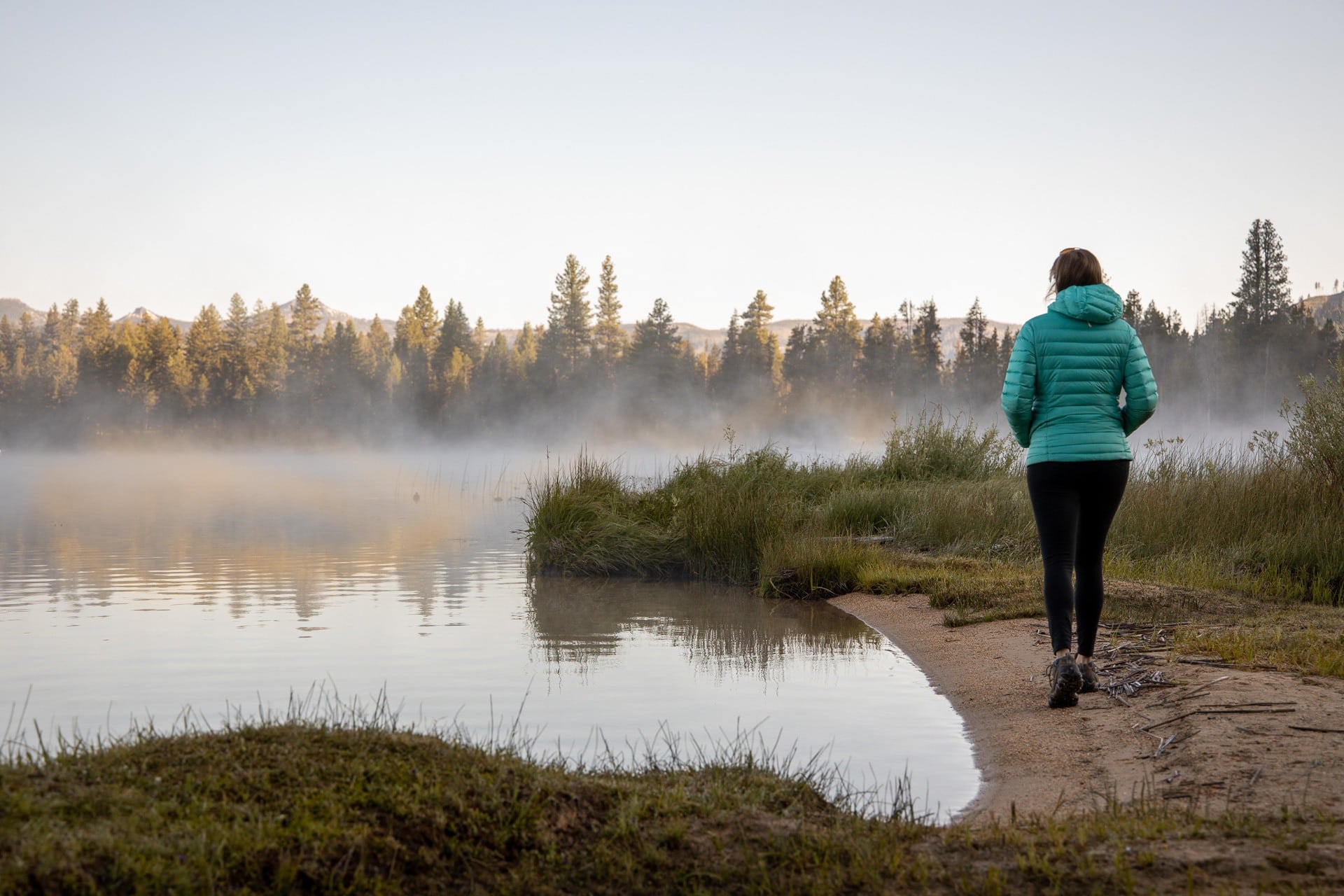 Kristen walking away from camera on shore of lake in the fall with mist over water