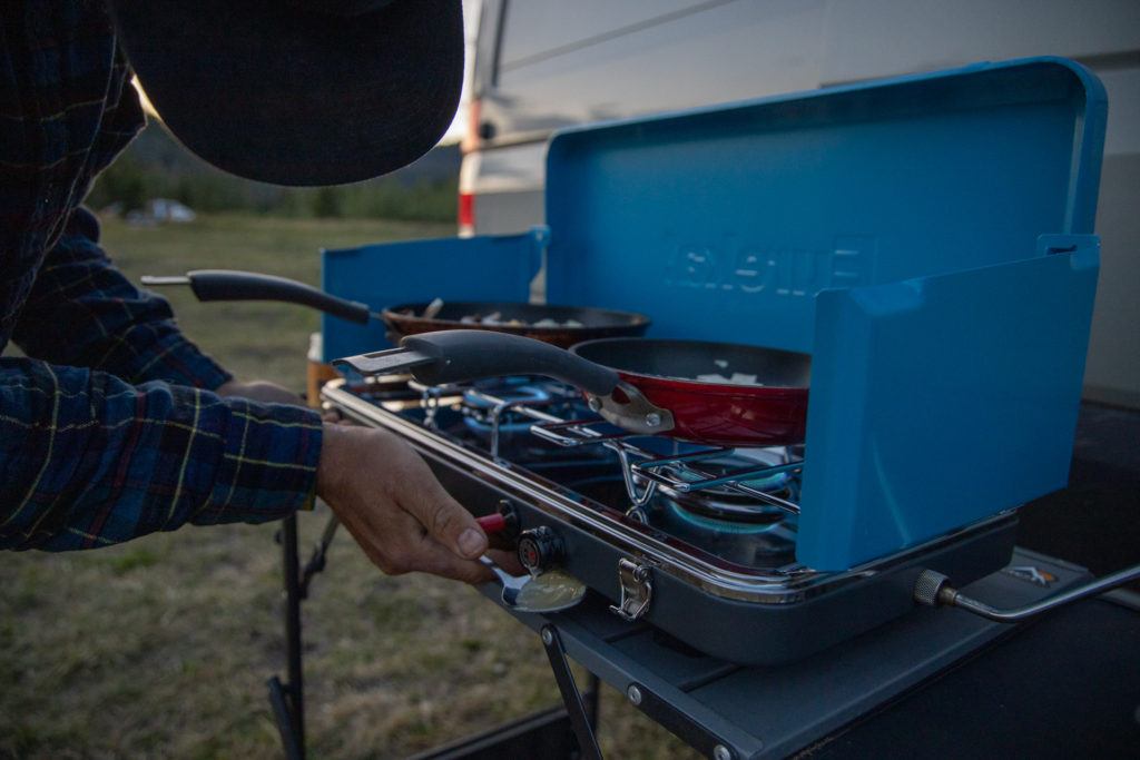 Camper turning on propane camp stove to cook camp meal