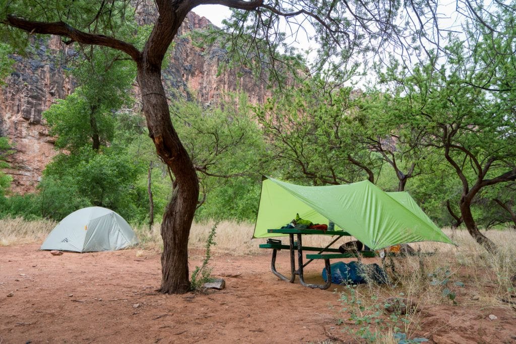 A backpacking tent set up near a picnic table with a tarp set up over it in the Havasu Falls campground