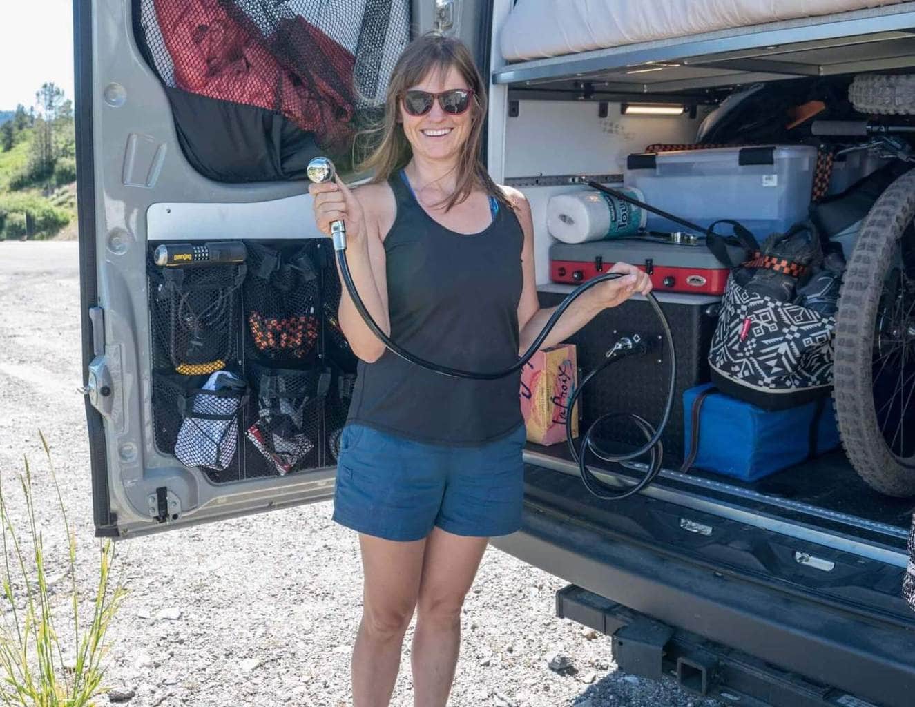 Kristen standing at rear of converted Sprinter van holding shower hose