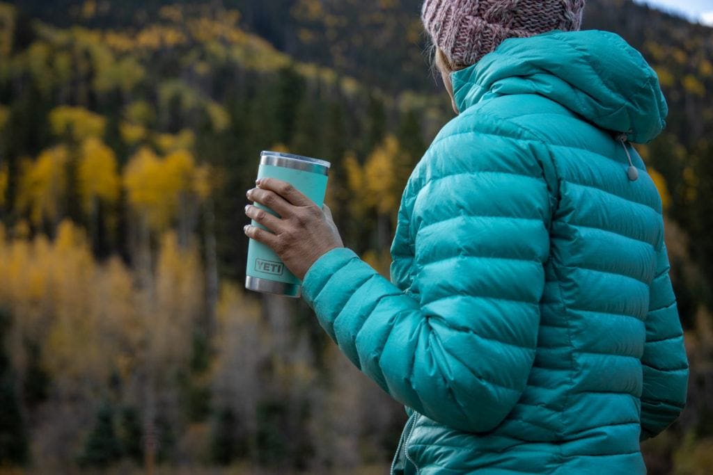 Woman wearing a teal puffy jacket and a beanie on a cold fall Colorado day holding an insulated YETI tumbler