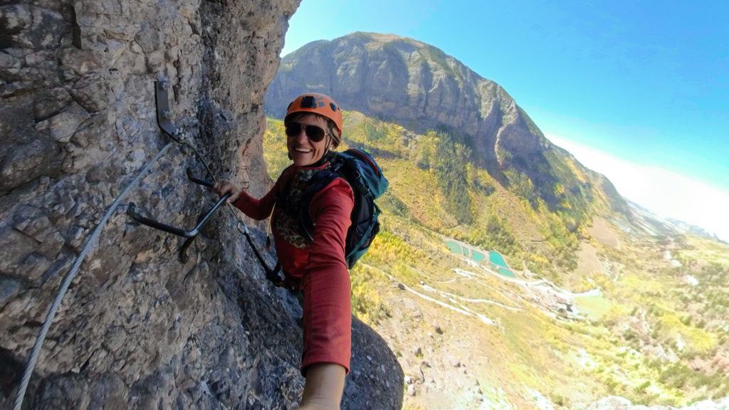 Kristen taking a selfie while holding onto a metal anchor on the Telluride Via Ferrata