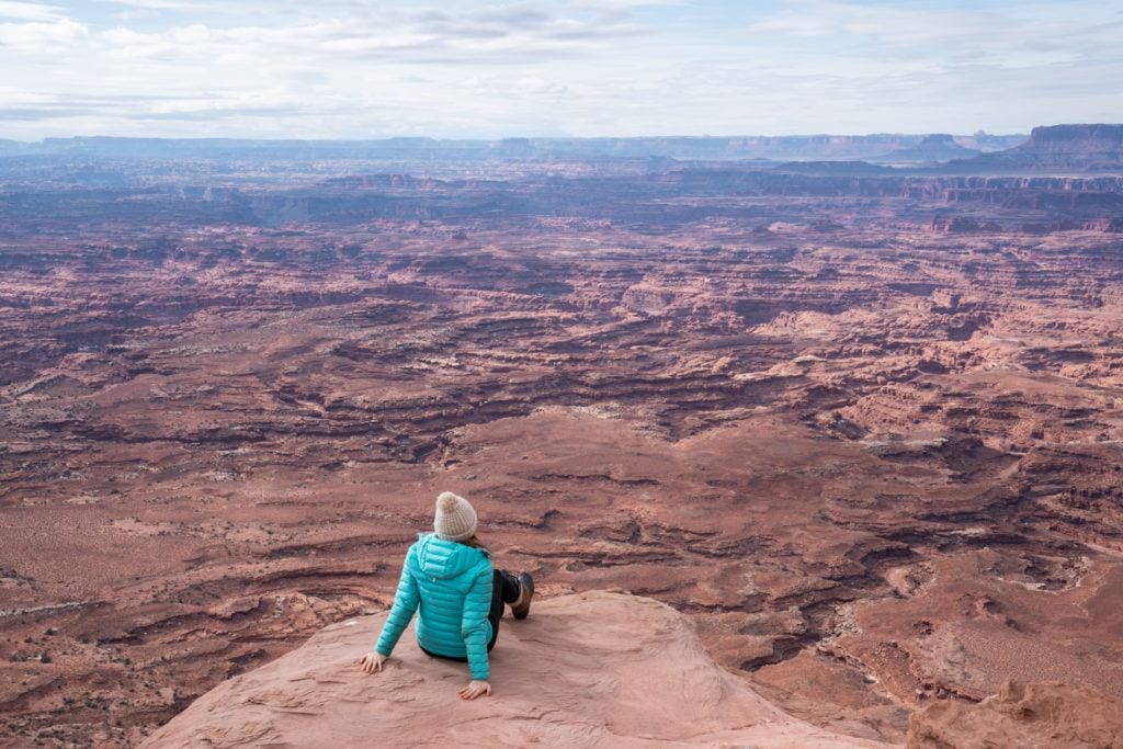 Woman sitting on rocky ledge overlook with expansive Utah Canyonlands below