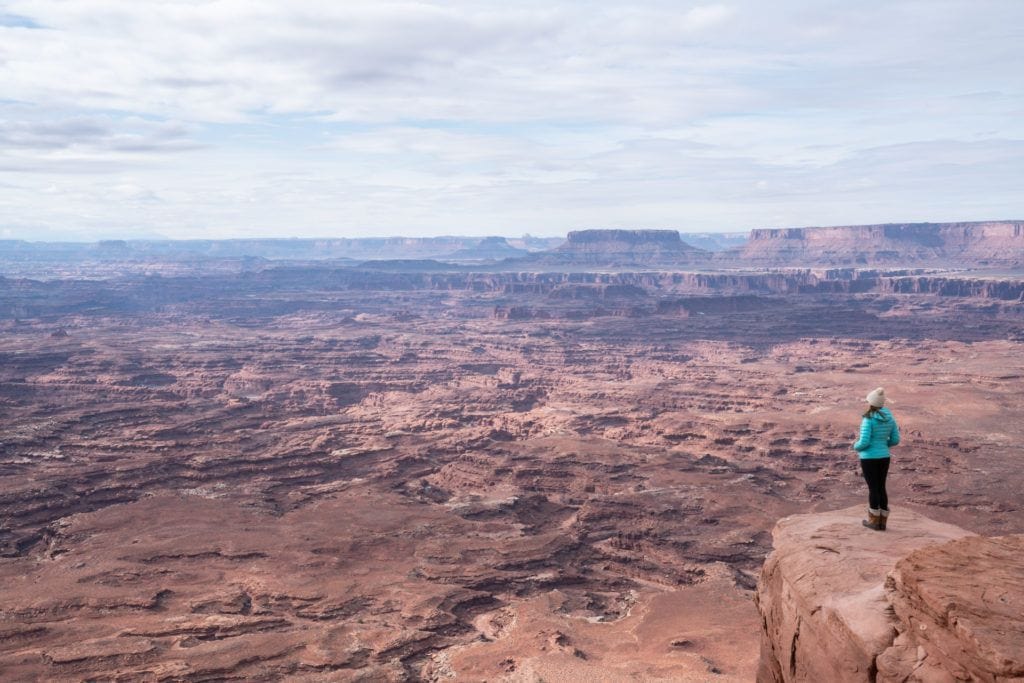 A woman stands on a rocky edge overlooking Canyonlands National Park