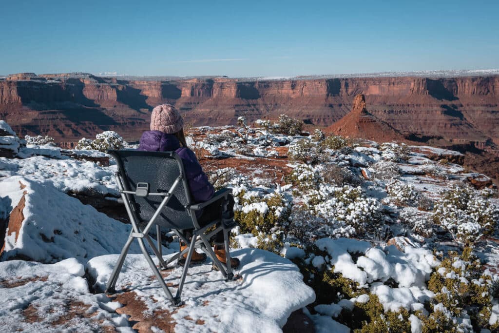 Woman sitting in camp chair at scenic canyonland overlook outside of Moab. Ground is covered in snow