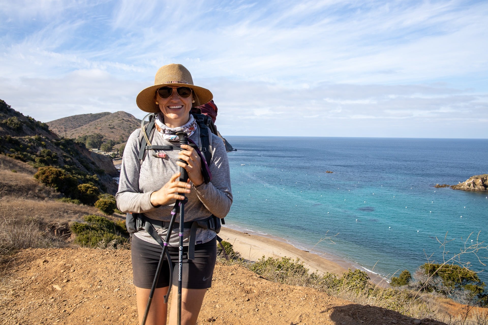 A woman holding trekking poles smiling on a coastal hiking trail