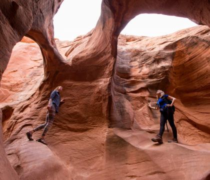 Two women exploring red rock cave with three sky holes in Utah
